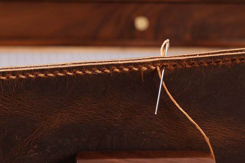 May include: Close-up of a brown leather item being sewn with a needle and tan thread.
