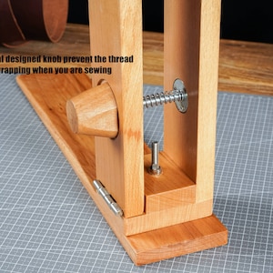 May include: A wooden leathercraft stitching pony with a special knob to prevent thread wrapping. The tool is made of light-coloured wood and features a metal spring and bolt. The text on the image reads: "Special designed knob prevent the thread from wrapping when you are sewing."