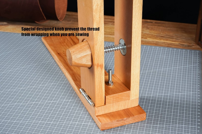 May include: A wooden leathercraft stitching pony with a special knob to prevent thread wrapping. The tool is made of light-coloured wood and features a metal spring and bolt. The text on the image reads: "Special designed knob prevent the thread from wrapping when you are sewing."