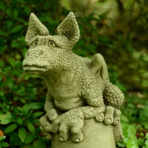 May include: A small, green, stone dragon statue with a textured surface. The dragon is sitting on a round, stone base.