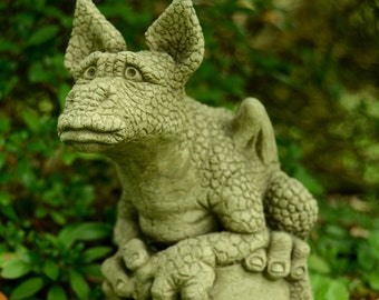 May include: A small, green, stone dragon statue with a textured surface. The dragon is sitting on a round, stone base.
