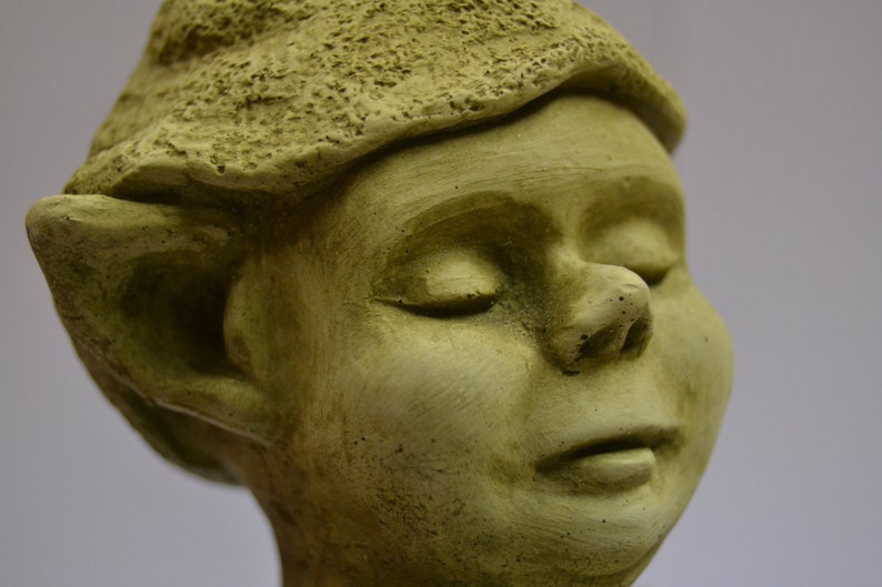 Puede incluir: Primer plano de una escultura de piedra verde de un rostro humano con los ojos cerrados. La escultura tiene una textura detallada y una nariz ligeramente hacia arriba.