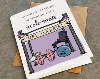 May include: A white greeting card featuring a cartoon illustration of a pink dumbbell wearing a floral veil and a blue kettlebell wearing a top hat and bowtie. The text reads CONGRATULATIONS ON FINDING YOUR swole-mate and JUST MARRIED.