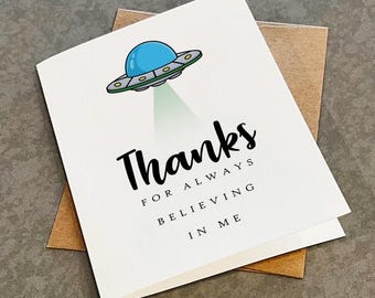 May include: A white card with a cartoon UFO and the text "Thanks for always believing in me".