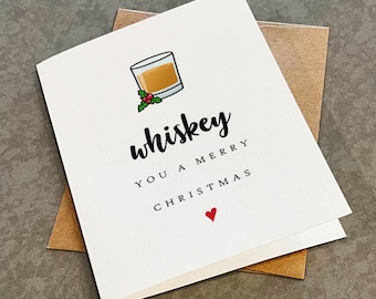 May include: A white greeting card featuring a cartoon illustration of a glass of amber whiskey with a sprig of holly. The text reads "whiskey YOU A MERRY CHRISTMAS" in black lettering, accompanied by a small red heart symbol at the bottom center.