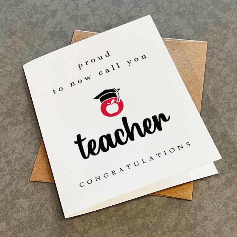 Puede incluir: Una tarjeta blanca con texto negro que dice "Orgulloso de poder llamarte profesor ahora Felicitaciones". Una manzana roja con un gorro de graduaci&oacute;n negro en la parte superior est&aacute; en el centro de la tarjeta.