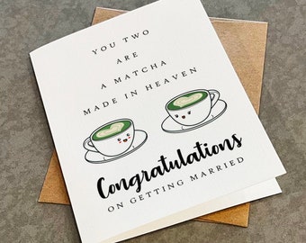 May include: A white card with the text "You two are a matcha made in heaven" and two cartoon cups of matcha with hearts and smiley faces. The text "Congratulations on getting married" is written below the cups.
