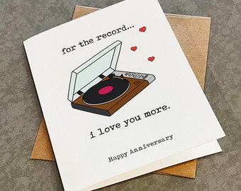 Peut inclure: Une carte blanche avec une illustration noire et brune d'un tourne-disque avec le texte "for the record..." et "i love you more." La carte contient également des cœurs rouges et le texte "Happy Anniversary".
