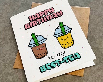 May include: A white card with the text "Happy Birthday to my Best-Tea" in colourful letters. Two cartoon bubble tea cups with smiling faces are on the card.