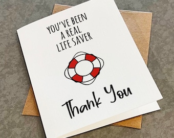 May include: A white greeting card with the text "YOU'VE BEEN A REAL LIFE SAVER" and "Thank You" in black script. A red and white life preserver graphic is centered on the card. The card is paired with a brown envelope.
