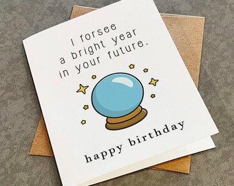 May include: A white card with a blue and gold magic eight ball illustration and the text "I foresee a bright year in your future. happy birthday".