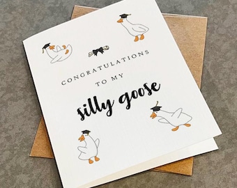 May include: A white greeting card with a brown envelope featuring four illustrations of white geese wearing black graduation caps. The text reads CONGRATULATIONS TO MY silly goose in black lettering, accompanied by a small black diploma illustration.