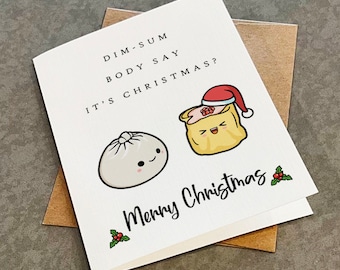 May include: A white greeting card featuring a cartoon illustration of a steamed bun and a dumpling wearing a red Santa hat. The text reads: DIM-SUM BODY SAY IT'S CHRISTMAS? and Merry Christmas with small holly illustrations. A brown envelope is underneath.