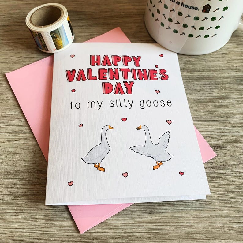 May include: A white card with pink hearts and the text "Happy Valentine's Day to my silly goose" in red letters. Two white geese are illustrated on the card, one facing left and the other facing right.