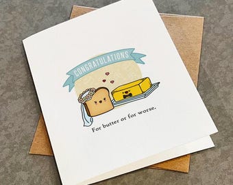 May include: A white greeting card featuring a cartoon illustration of a slice of toast wearing a floral veil and a stick of butter wearing a bow tie. Above them is a blue banner with the text CONGRATULATIONS and below is the text For butter or for worse.