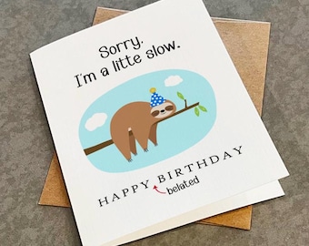 May include: A white greeting card featuring a brown sloth wearing a blue and yellow party hat while hanging on a tree branch. The text reads, Sorry. I'm a litte slow. HAPPY BIRTHDAY with the word belated written below with a red arrow.
