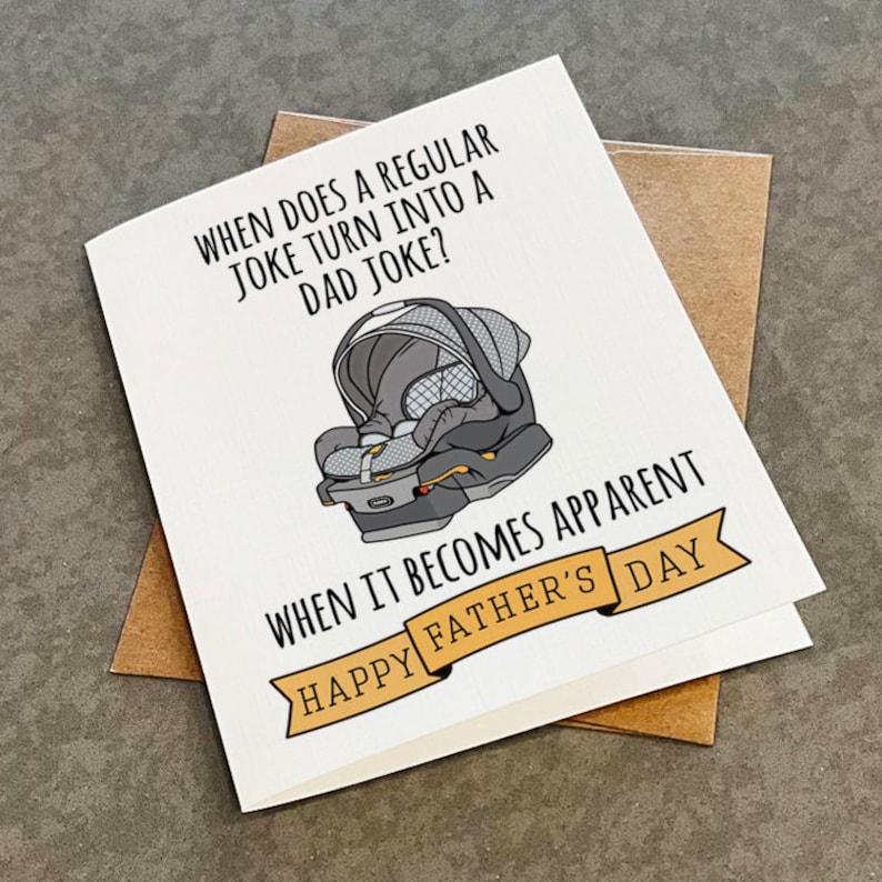 May include: A white card with a black and gray illustration of a baby car seat. The card has the text "When does a regular joke turn into a dad joke? When it becomes apparent. Happy Father's Day."