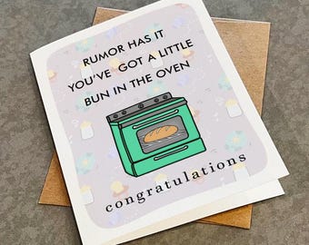 May include: A white card with a green oven illustration and the text "Rumour has it you've got a little bun in the oven. Congratulations."