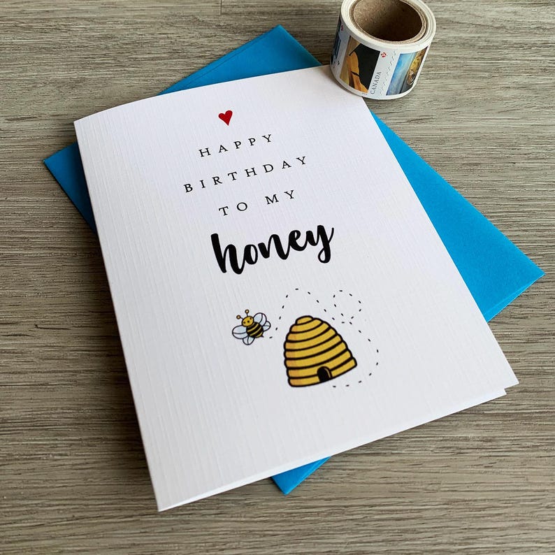 May include: A white card with a red heart, black text that reads "Happy Birthday to my honey", and a cartoon bee and beehive.