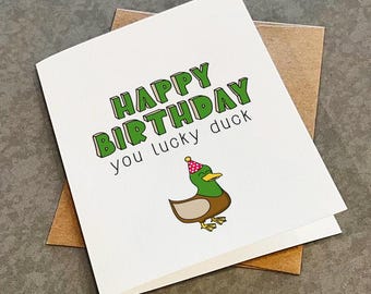 May include: A white card with green text that reads "Happy Birthday you lucky duck". A cartoon duck wearing a pink and white party hat is illustrated below the text.