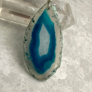 May include: A teal blue agate pendant with a silver bail. The agate has a white center and a teal blue outer edge.