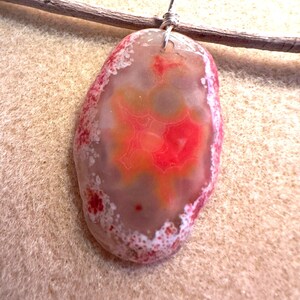 May include: A pendant made from a slice of agate with a red, orange, and white pattern. The agate is attached to a silver wire loop.