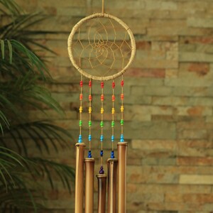 May include: A handcrafted dreamcatcher with a woven circular frame and colorful beaded strands. The dreamcatcher hangs from a string, with bamboo chimes suspended below. The chimes are various shades of brown and tan, creating a natural, earthy aesthetic.