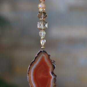 May include: A brown agate slice with a white and orange pattern hangs from a gold chain with clear and amber glass beads.