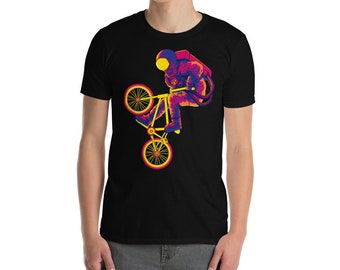 Puede incluir: Una camiseta negra con un gráfico de un astronauta montando una bicicleta en un esquema de colores amarillo, rojo y azul.
