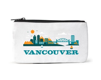 Puede incluir: Una bolsa de lona blanca con cremallera que presenta una ilustración colorida del horizonte de Vancouver, que incluye montañas, edificios, un puente y un velero. El texto "VANCOUVER" está impreso en letras azules negritas debajo de la ilustración.