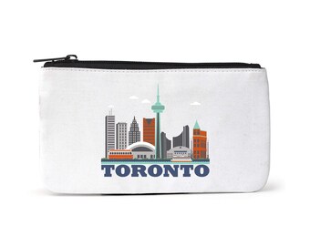 Puede incluir: Bolsa de lona blanca con cremallera negra. La bolsa presenta una ilustración colorida del horizonte de Toronto con la palabra "TORONTO" impresa en azul debajo de la imagen.