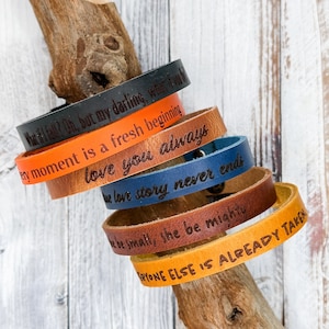May include: A stack of six leather bracelets with different engraved messages. The messages include "What if I fall? Oh, but my darling, what if I fly?", "Every moment is a fresh beginning", "Love you always", "True love story never ends", "Be small, she be mighty", and "Everyone else is already taken."