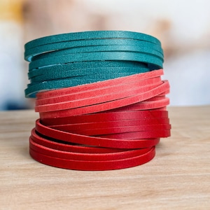 May include: A stack of leather strips in teal, coral, and red colors. The strips are rolled up and stacked on top of each other.