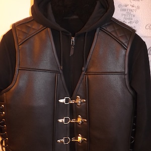 May include: Black leather vest with a quilted design and silver buckles. The vest has a zipper closure and a hood.