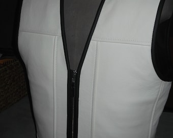 May include: White leather vest with a black zipper and black trim. The vest has a V-neck and is made of a soft, supple leather.