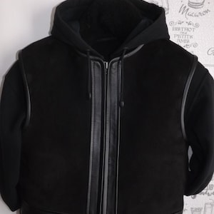 Può includere: Giacca nera con cappuccio e bordi in pelle sui bordi e sulla cerniera anteriore. La giacca è foderata in pile.