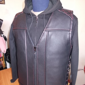 Puede incluir: Chaleco de cuero negro con cierre de cremallera y costuras rojas. El chaleco tiene un diseño acolchado en los hombros y un detalle de encaje en los lados.