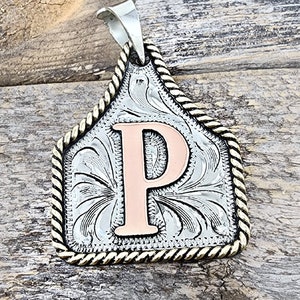May include: Silver and gold-toned metal pendant with a rope-like border. The pendant features a copper-colored letter "P" in the center.