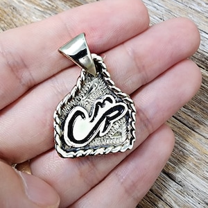 May include: A gold-toned pendant with a rope-like border and the initials "CR" in black lettering.