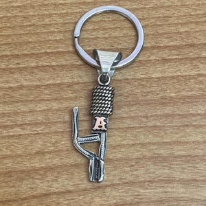 Puede incluir: Llavero de metal plateado con un anillo, una secci&oacute;n trenzada y un elemento decorativo con la letra "A". El llavero est&aacute; dise&ntilde;ado con una apariencia detallada y texturizada.
