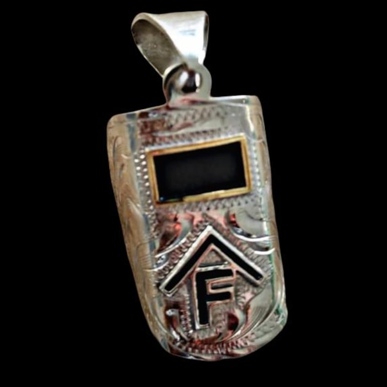 May include: Silver pendant with a rectangular shape, featuring a black rectangle framed in gold. The pendant has an engraved design and a stylized house and the letter "F" in black. The bail is silver.
