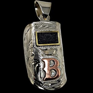 May include: Silver pendant shaped like a welding mask, featuring intricate floral engraving. The mask has a black rectangle with a gold border and a copper-colored letter "B". The pendant hangs from a silver bail.