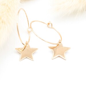 Peut inclure: Boucles d'oreilles créoles dorées avec un charme étoile suspendu à chaque créole.