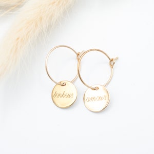 Peut inclure: Boucles d'oreilles créoles en or avec de petits pendentifs ronds gravés "bonheur" et "amour".