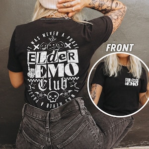 May include: Black t-shirt with white text that reads "It was never a phase Elder Emo Club". The text is surrounded by a skull and crossbones, flowers, and stars. The shirt is being modeled by a person with tattoos.