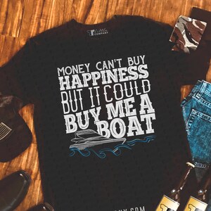 May include: Black t-shirt with white text that reads "Money can't buy happiness but it could buy me a boat". A white boat with blue waves is pictured below the text. The shirt has a small white tag with the text "R Little Company" on the upper left side.