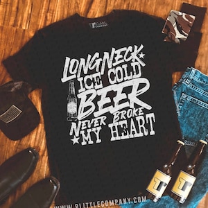 May include: Black t-shirt with white text that reads "Long Neck Ice Cold Beer Never Broke My Heart". The shirt features a graphic of a bottle of beer.