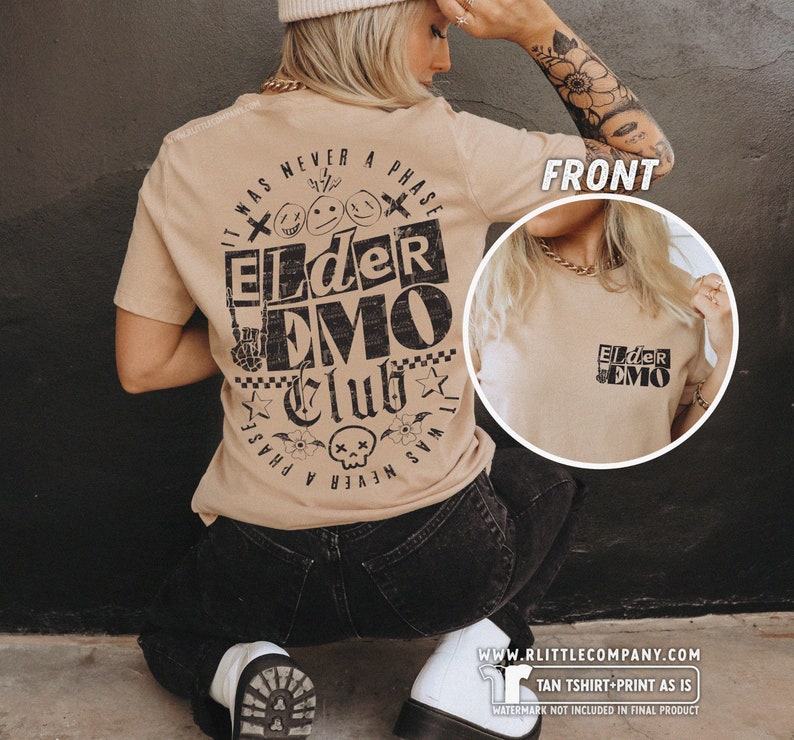 May include: Tan t-shirt with a black graphic print that says "It was never a phase Elder Emo Club" with a skull and crossbones, flowers, and stars. The front of the shirt has a smaller version of the graphic that says "Elder Emo".