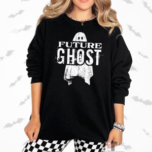 May include: Black long-sleeve sweatshirt with the text "FUTURE GHOST" and a ghost graphic. The sweatshirt is worn with black and white checkered pants. The image has a Halloween theme.