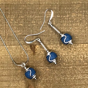May include: A set of silver earrings and a necklace with blue lava rock beads. The beads are wrapped in silver wire.